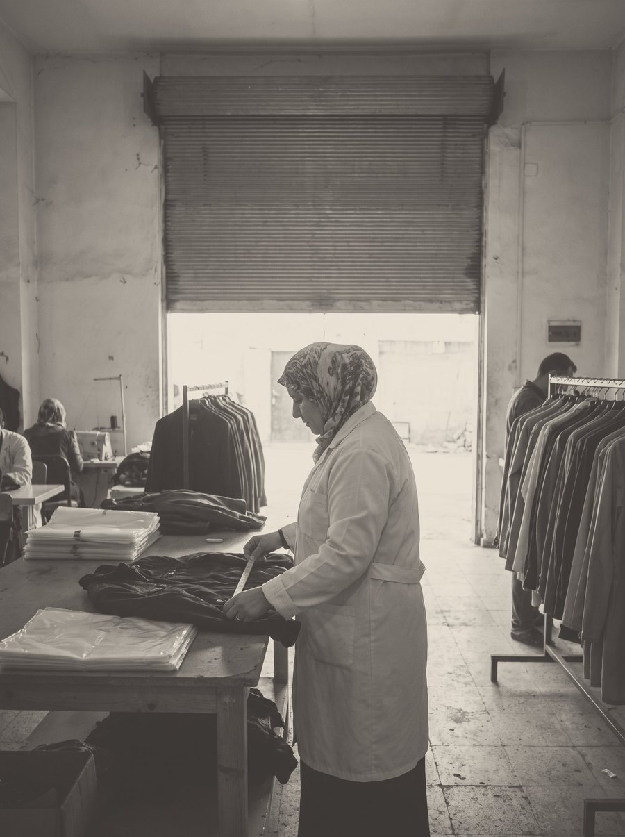 A checker with a clipboard inspects a finished jacket on the rail.